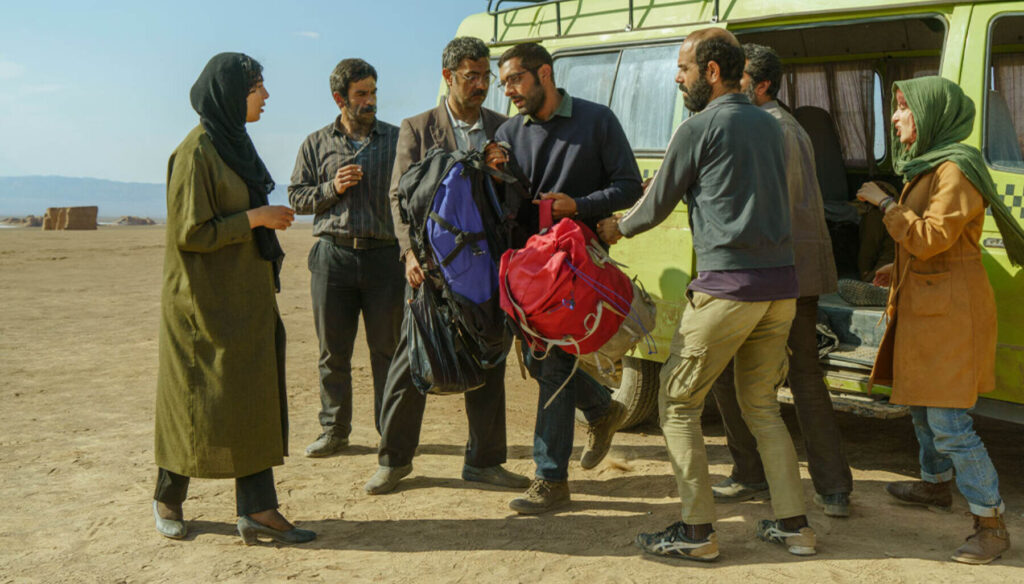 Still from the Iranian film "Cause of Death: Unknown" directed by Ali Zarnegar, showing the passengers gathered beside a green van in the desert near Kerman.